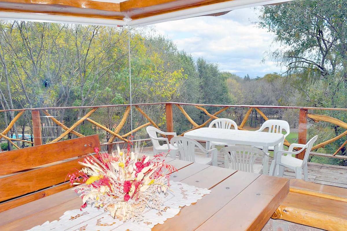 An outdoor dining area with wooden tables and white plastic chairs, surrounded by a wooden deck with a railing.