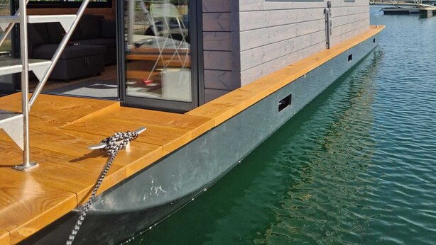 Una vivienda flotante moderna con terraza de madera, una escalera que lleva a una puerta de cristal y vistas al agua.
