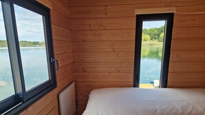 Una habitación de cabaña de madera con una cama, una ventana y vista a un lago.