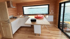 Cocina compacta con un ventanal grande que ofrece vistas al agua, paredes de madera y un pequeño comedor.