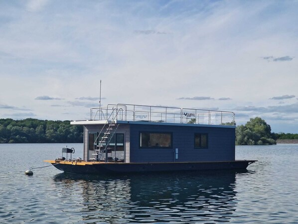 Una casa flotante con cubierta, una pequeña cabaña y una escalera visible.