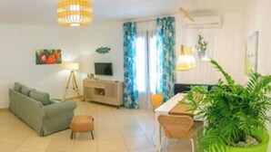 Una sala de estar con sofá, una mesita, lámpara, televisor y una planta.