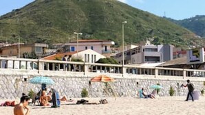 Una playa con un muro de piedra, sombrillas y edificios al fondo.