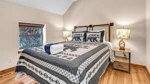 Een slaapkamer met een groot bed, twee bedlampen, een raam met uitzicht op bomen en een plafondventilator.