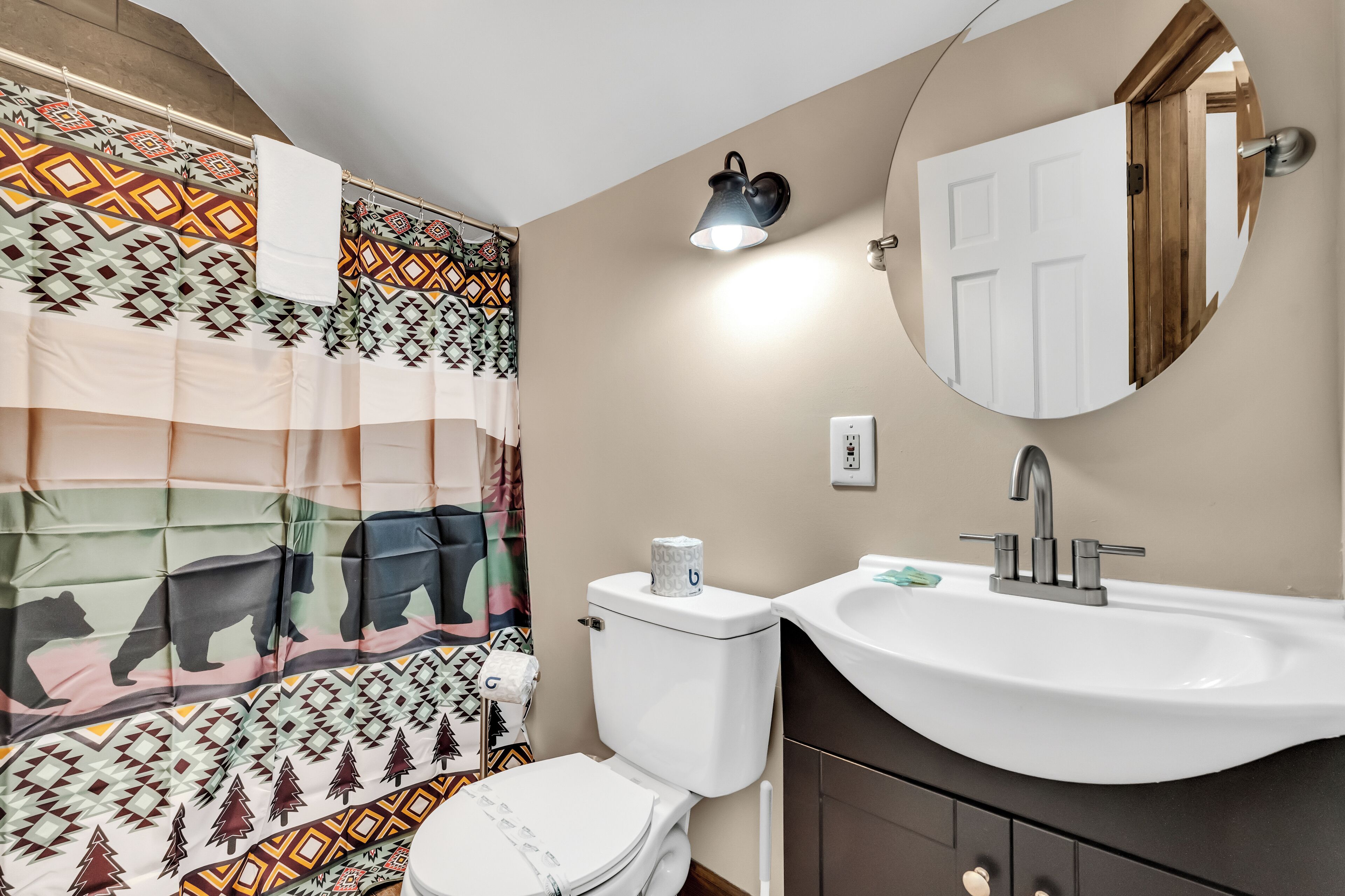 A bathroom with a patterned shower curtain, a toilet, a sink, and a mirror.