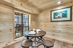 A wooden interior with a round table, chairs, and a framed picture on the wall.