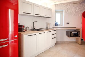 A kitchen with white cabinets, a red refrigerator, a microwave, and a window with a view.