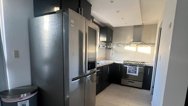 A modern kitchen with stainless steel appliances, a trash bin, and a tiled floor. - Casa Madeira (Mexicali)