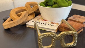 A wooden bowl with green felt balls, a pair of glasses, and a book titled "ON BOWERS" on a dark wooden table. - Modern 2BR Retreat - Fast WiFi, AC & Prime Houston Location (Houston)