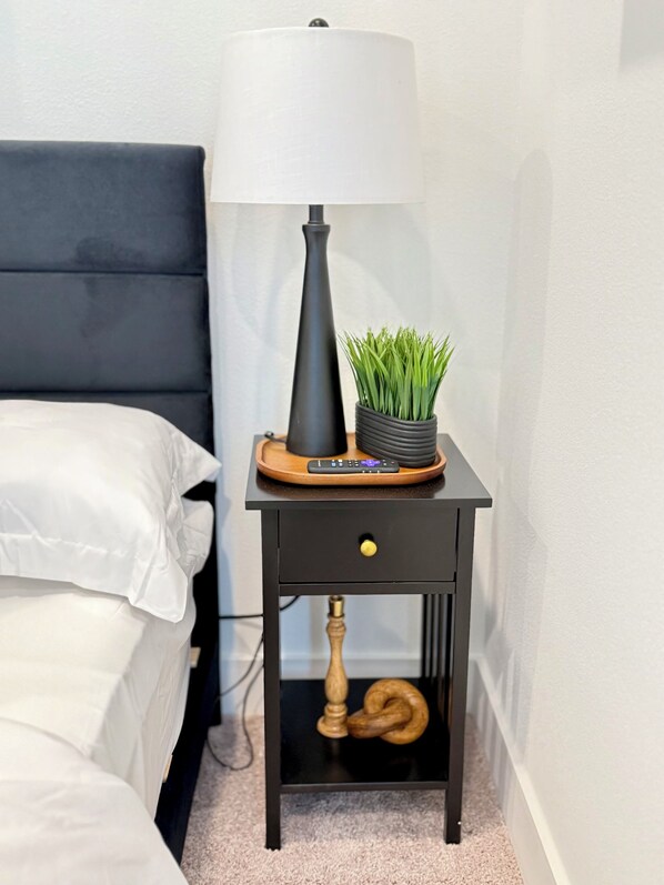A small bedside table with a lamp, a remote control, and a potted plant.