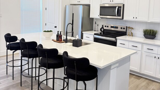 A modern kitchen with white cabinets, a central island with bar stools, stainless steel appliances, and pendant lighting. - Modern 2BR Retreat - Fast WiFi, AC & Prime Houston Location (Houston)