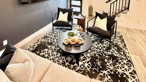 A modern living room with a ceiling fan, a flat-screen TV mounted on the wall, a staircase leading to another level, and a patterned rug. - Modern 2BR Retreat - Fast WiFi, AC & Prime Houston Location (Houston)