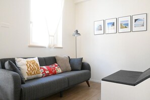 Un salon moderne avec un canapé gris, une petite table, un lampadaire et une fenêtre ornée de rideaux légers.