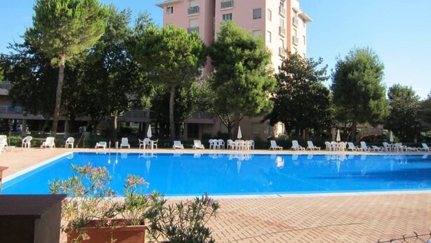 A swimming pool with lounge chairs, surrounded by trees and a multi-story building. - M434 – Marcelli, three-Room Apartment in Residence with Pool (Marcelli)