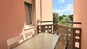 A balcony with a table and chairs, a window with blinds, and a view of greenery. - M434 – Marcelli, three-Room Apartment in Residence with Pool (Marcelli)