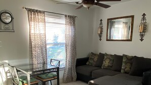 A living room with a ceiling fan, a sofa, a dining table with chairs, and a window with curtains.