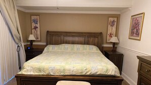 A bedroom with a large bed, a wooden headboard, a bench, two bedside tables with lamps, and a dresser.