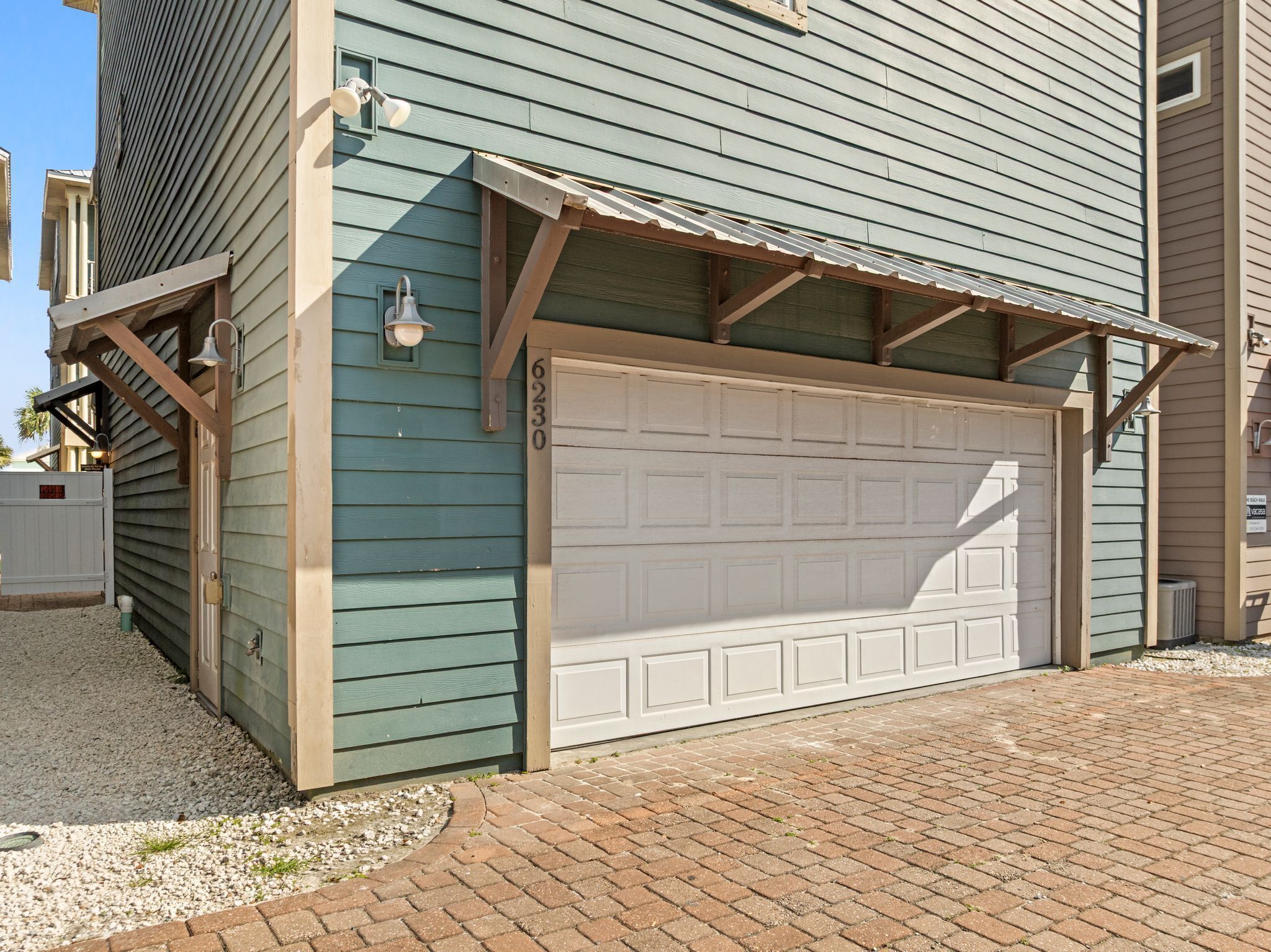 A two-story building with a garage door, a small porch with a railing, and a mailbox.