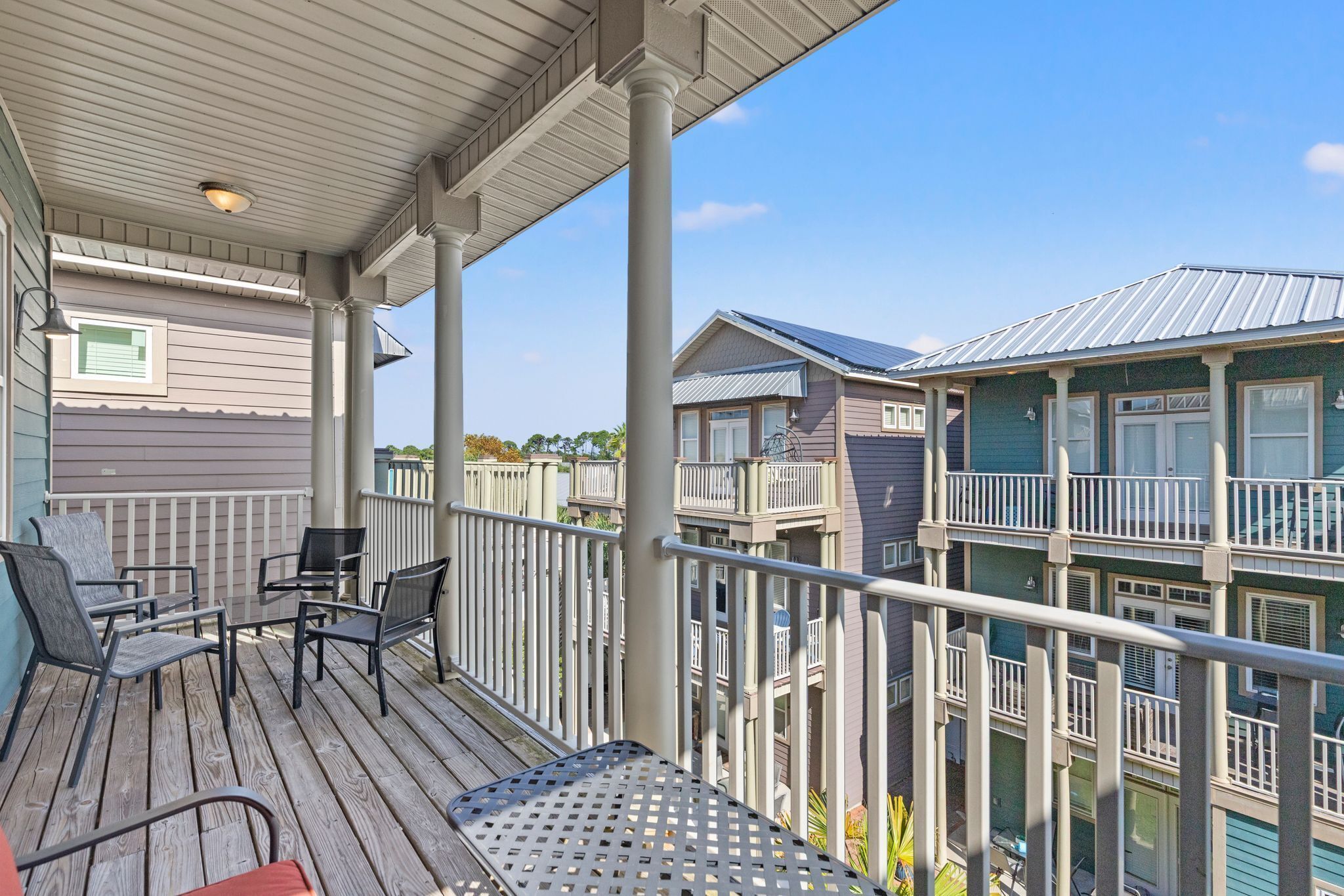 Une terrasse en bois avec des meubles d’extérieur, un espace couvert avec un luminaire au plafond et une vue sur des immeubles à plusieurs étages dotés de balcons.