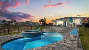 Una piscina con hidromasaje, un porche cubierto con sillas y vistas al atardecer.