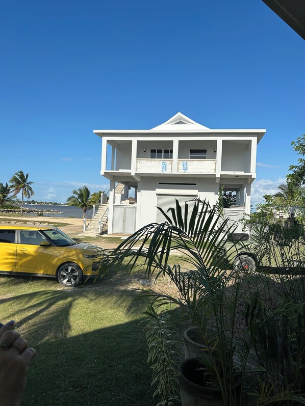 A two-story house with a garage, a yellow car parked in front, and a view of the ocean.