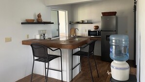 A compact kitchen with a central island, two chairs, a water dispenser, and a refrigerator. - Bay Front Eco-Cottage/2 units/Corozal with WiFi, AC (Corozal)