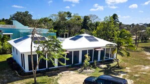 A two-story house with a white exterior and solar panels on the roof. - Bay Front Eco-Cottage/2 units/Corozal with WiFi, AC (Corozal)