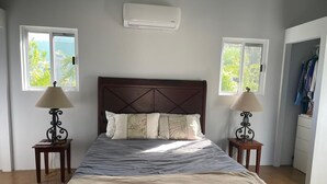 A bedroom with a bed, two bedside tables with lamps, a window, and an air conditioning unit. - Bay Front Eco-Cottage/2 units/Corozal with WiFi, AC (Corozal)