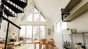 A spacious living area with a high ceiling, a staircase, a dining table with chairs, and a bookshelf. - Modern Alpine Cabin in Twin Lakes (Twin Lakes)