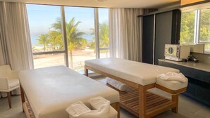 A spa room with two massage tables, a small seating area, and a view of the beach. - Hotel Nacional (Rio de Janeiro)