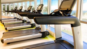 A row of treadmills with digital displays, positioned in a room with large windows overlooking a scenic view. - Hotel Nacional (Rio de Janeiro)
