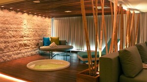 A modern, well-lit room with a stone wall, a round table, and a sofa. There is a small table with a bowl and a plant. - Hotel Nacional (Rio de Janeiro)
