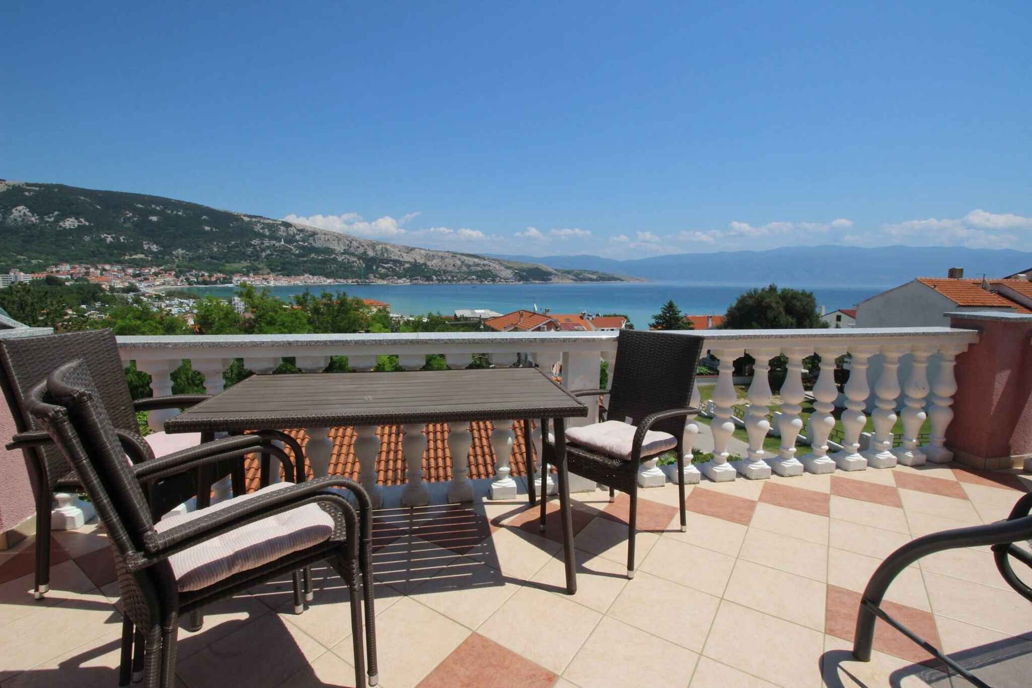 A balcony with a table and chairs, offering a view of a coastal town and the sea.