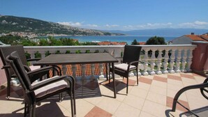 Ein Balkon mit Tisch und Stühlen, der Blick auf eine Küstenstadt und das Meer gewährt.