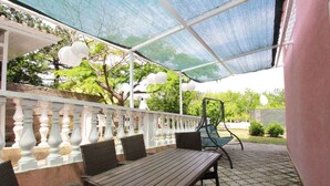 Ein überdachter Patio-Bereich mit Holztisch und -stühlen, einem weißen Geländer und Blick ins Grüne.