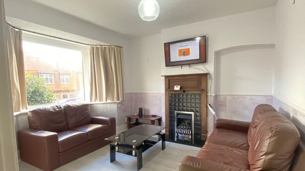 A living room with two brown leather sofas, a glass coffee table, a fireplace, and a television mounted on the wall.
