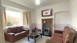A living room with two brown leather sofas, a glass coffee table, a fireplace, and a television mounted on the wall.