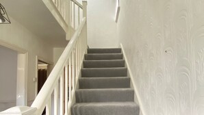 A staircase with white railings and grey carpeted steps leading to a landing.