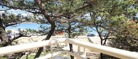 A balcony with a white railing overlooking a parking area and a body of water.