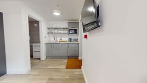 Una cocina moderna con armarios grises, un horno empotrado y un microondas. El suelo es de madera y hay una alfombra marrón en el pasillo.