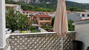 Un balcon agrémenté d’un parasol beige, d’une clôture en treillis et offrant une vue sur un quartier résidentiel, avec des maisons et des montagnes en arrière-plan.