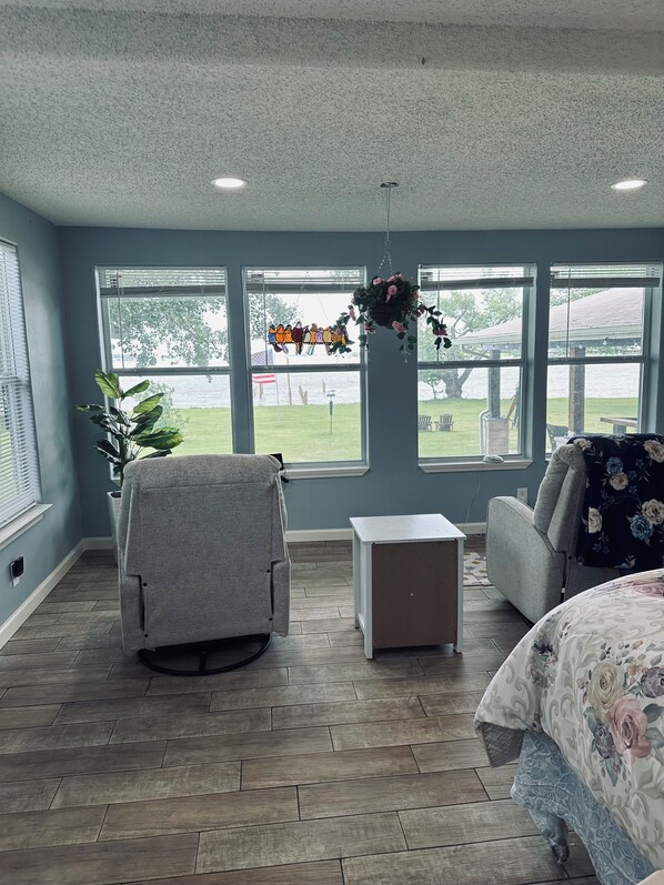 A room with a large window, a chair, a small table, and a bed.