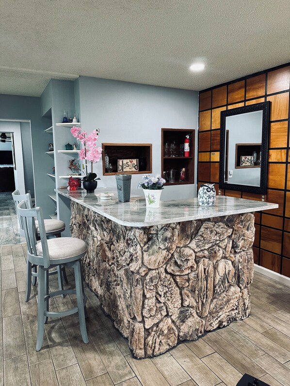 Una cocina con una isla de piedra, taburetes de bar y estantes con objetos decorativos.