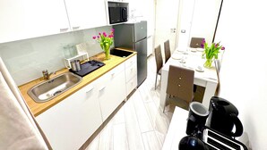Una cocina moderna con armarios blancos, un lavamanos de acero inoxidable, un microondas y un refrigerador. Hay dos jarrones con flores sobre la encimera.