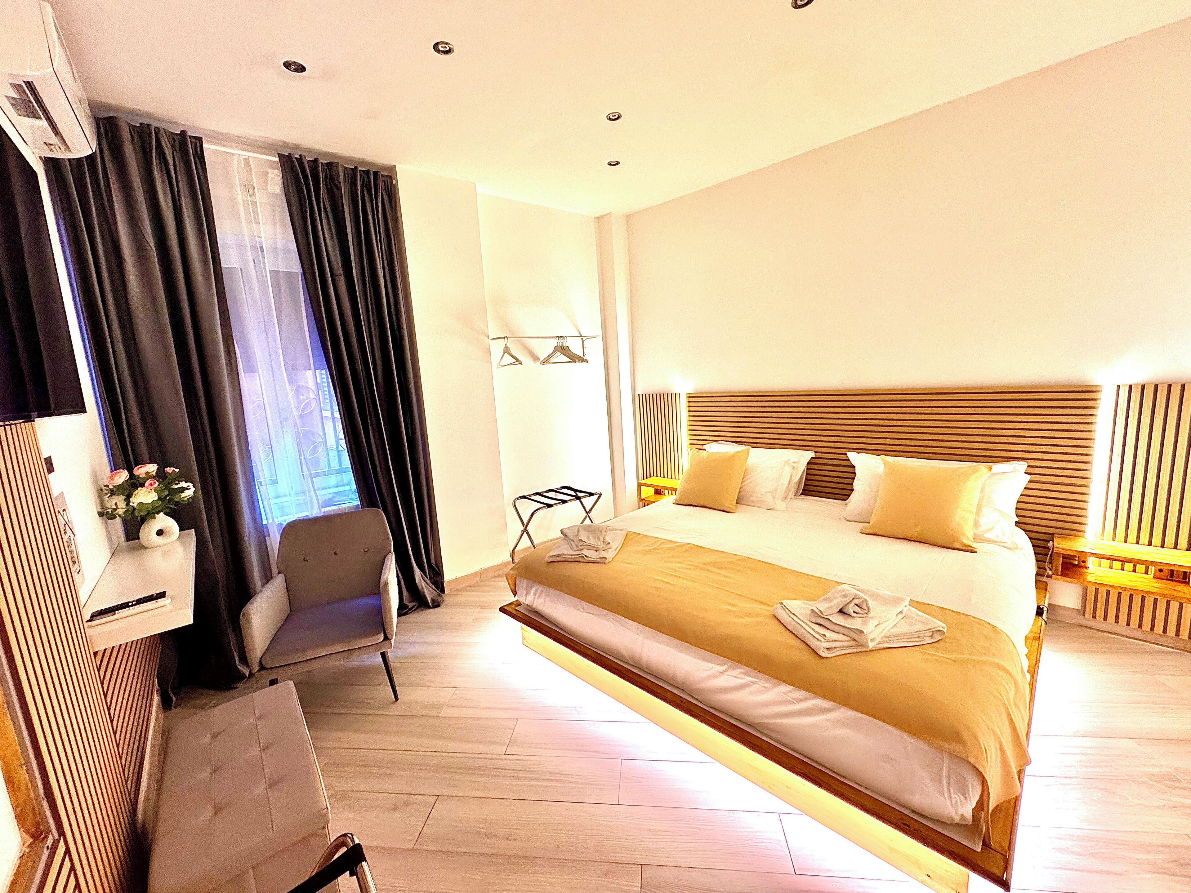 A hotel room with a large bed, a chair, a desk, and a window with curtains.