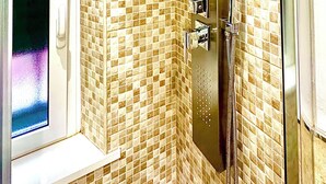 Una ducha con mampara de vidrio, paredes con azulejos y un cabezal de ducha manual.