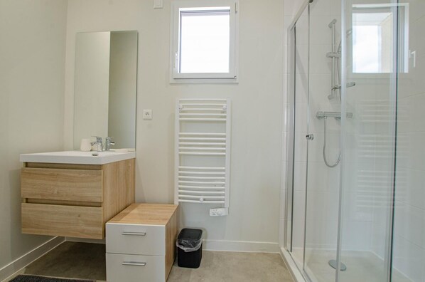 A modern bathroom with a wooden vanity, a glass shower enclosure, and a window providing natural light.
