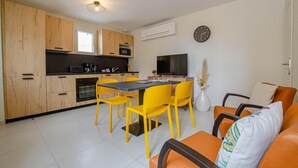 A modern kitchen with wooden cabinets, a dining area with yellow chairs, and a living space with orange furniture. - Number 1 - MORVILLIERS (MORVILLIERS)