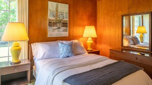 Une chambre d’hôtel avec des boiseries, un lit recouvert de draps blancs, deux lampes de chevet, un miroir et un tableau encadré au mur.
