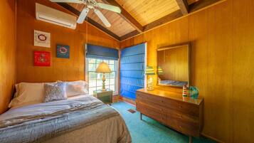 Een slaapkamer met een bed, een dressoir, een spiegel en een plafondventilator.